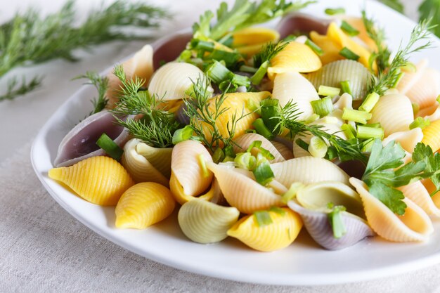 Pasta conchiglie coloreada con verdulería fresca sobre un mantel de lino