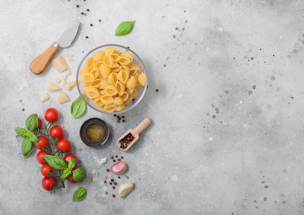 Pasta Conchiglie en recipiente de vidrio con queso parmesano y aceite de tomate y ajo con albahaca sobre fondo claro Espacio para texto