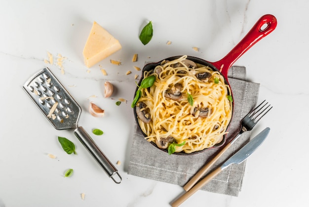 Pasta cremosa de champiñones con queso y albahaca, en sartén en porciones, sobre la mesa de mármol blanco vista superior