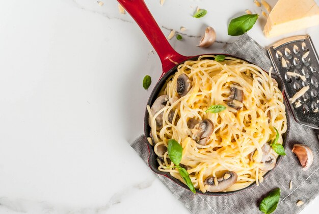 Pasta cremosa de champiñones con queso y albahaca, en sartén en porciones, sobre la mesa de mármol blanco vista superior