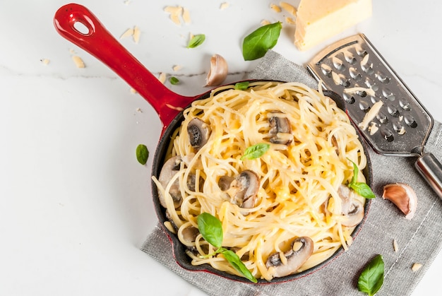 Pasta cremosa de champiñones con queso y albahaca, en sartén en porciones, sobre mesa de mármol blanco