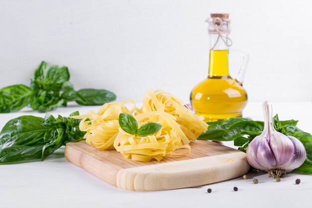 Pasta cruda y albahaca verde fresca con ajo en superficie blanca