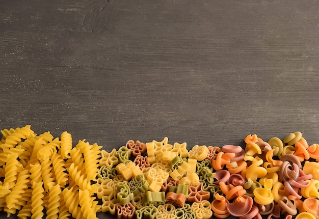 Pasta cruda de diferentes colores y tipos dispuestos en una mesa de madera oscura debajo