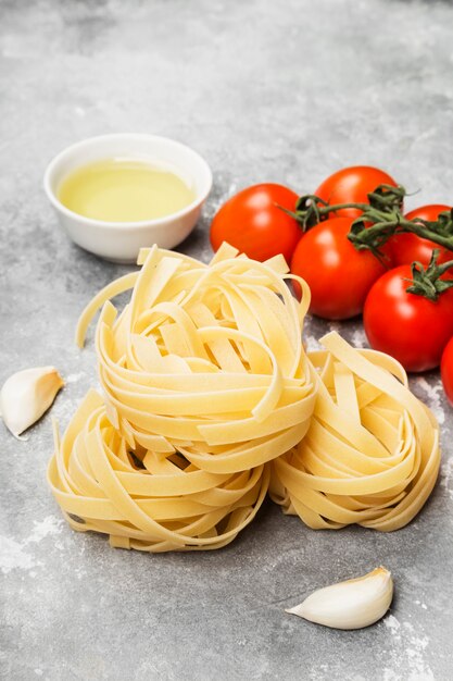Pasta cruda e ingredientes para cocinar (tomates, aceite de oliva, ajo) sobre fondo gris