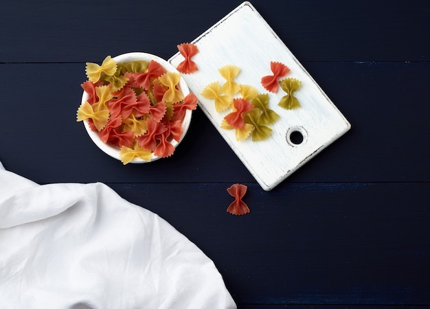 Foto pasta cruda en forma de arcos en un plato redondo de madera y servilleta textil blanca