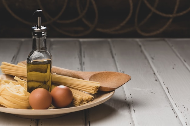 Foto pasta cruda con huevos y aceite en la mesa