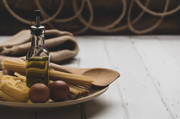 Foto pasta cruda con huevos y aceite en la mesa