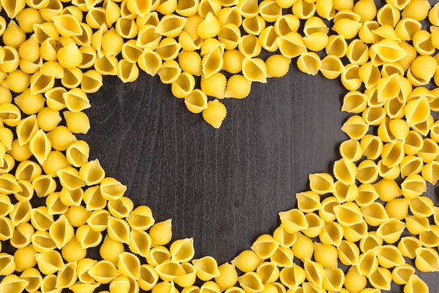 Foto pasta cruda de macarrones con un espacio vacío en forma de corazón sobre un fondo de madera