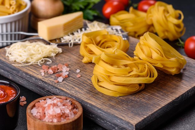 Pasta cruda de tagliatelle con queso rallado, tomates cherry, especias y hierbas en una tabla para cortar madera