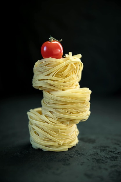 Pasta cruda de tallarines y tomate sobre el fondo de hormigón negro