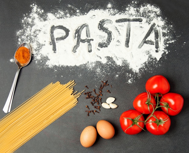 Pasta cruda, tomates, ajo, harina y huevos en la mesa de madera negra