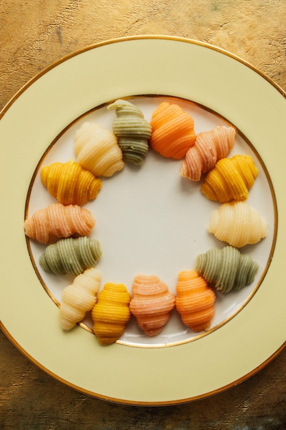 Pasta de conchas de mar coloridas cozidas em círculo em um prato amarelo dourado