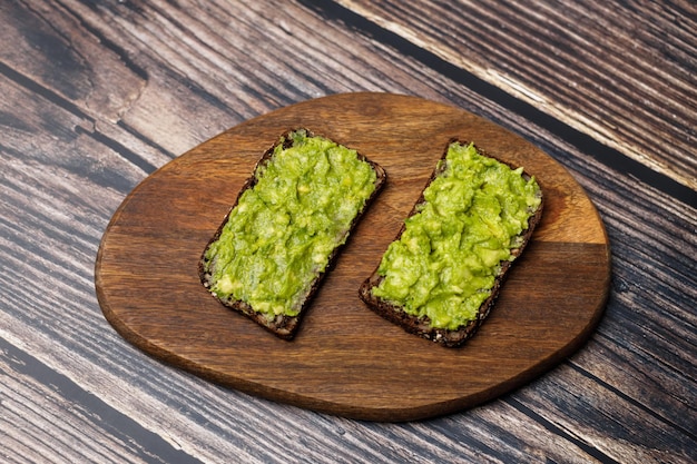 Pasta de guacamole e abacate são espalhadas em pão de centeio escuro deliciosa torrada de abacate na tábua