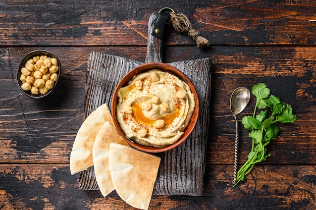 Pasta de homus com pão pita, grão de bico e salsa em uma tigela de madeira.