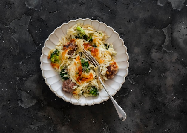 Pasta de orzo assada com almôndegas, brócolis, espinafre e queijo em um fundo escuro