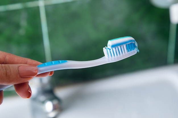 Pasta de dientes de mano de mujer en el cepillo de baño