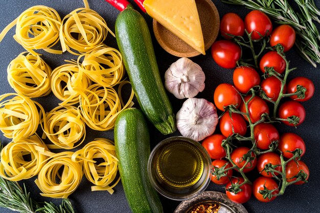 Pasta e ingredientes para cocinar en la superficie oscura, vista desde arriba. Pasta, tomates, ajo, romero, pimientos.