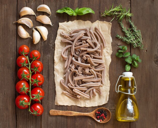 Pasta entera de espelta, verduras, hierbas y aceite de oliva sobre superficie de madera