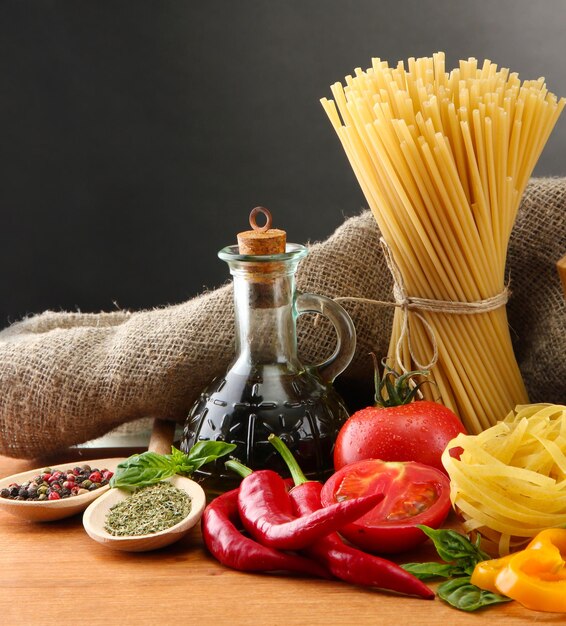 Foto pasta, espaguete, vegetais e especiarias em mesa de madeira sobre fundo cinzento