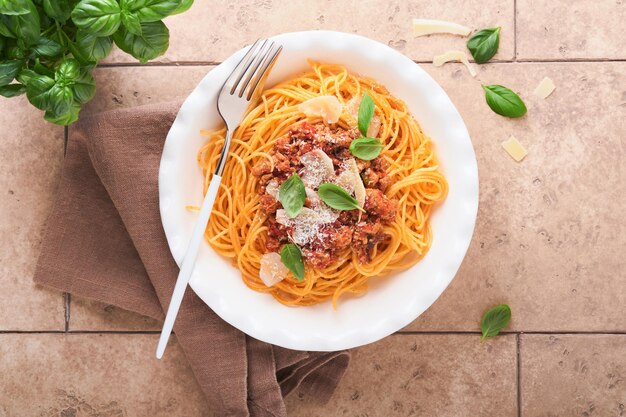 Pasta espagueti a la boloñesa Sabroso apetitoso espagueti italiano con salsa boloñesa salsa de tomate queso parmesano y albahaca en plato blanco sobre fondo de mesa de azulejos beige antiguo Vista superior