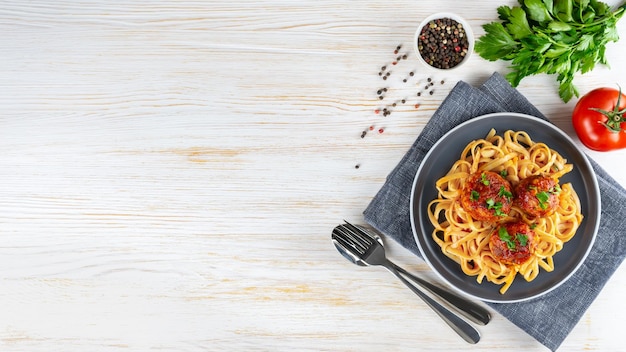 Pasta de espagueti casera con salsa de tomate, albóndigas y especias servidas sobre fondo blanco de madera