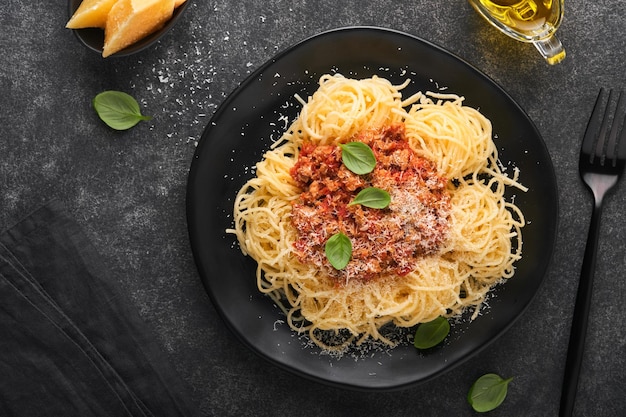 Pasta de espagueti clásica a la boloñesa Sabrosos y apetitosos espaguetis italianos con salsa boloñesa salsa de tomate queso parmesano y albahaca sobre plato negro sobre piedra oscura o fondo de mesa de hormigón Vista superior