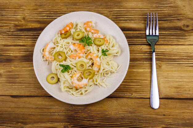 Pasta de espagueti con gambas, aceitunas verdes y perejil en la mesa de madera Vista superior