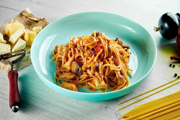 Pasta de espagueti italiano con salsa roja, pollo, champiñones y queso parmesano servido en un plato azul sobre una mesa de madera. Comida de restaurante.