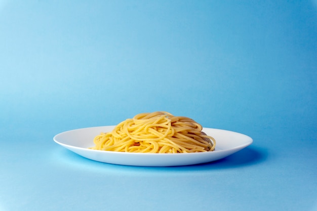 Pasta de espagueti en un plato blanco sobre un fondo azul