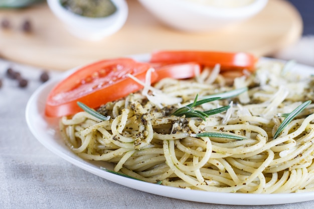 Pasta de espagueti con salsa de pesto, tomates y queso sobre un mantel de lino.