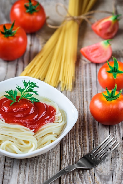 Pasta de espagueti con salsa de tomate en placa y tomates en mesa de madera.