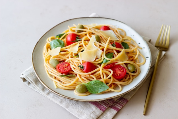 Pasta de espagueti con tomate, albahaca, aceitunas y queso parmesano. Alimentación saludable. Comida vegetariana.