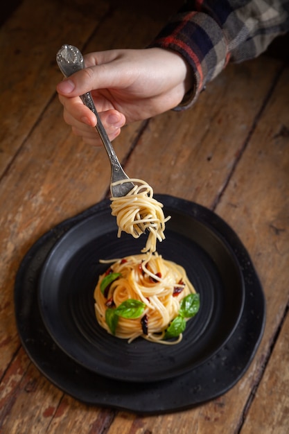 pasta de espagueti con verduras, pimienta, hojas de albahaca en un plato redondo negro sobre fondo de madera vintage rústico marrón