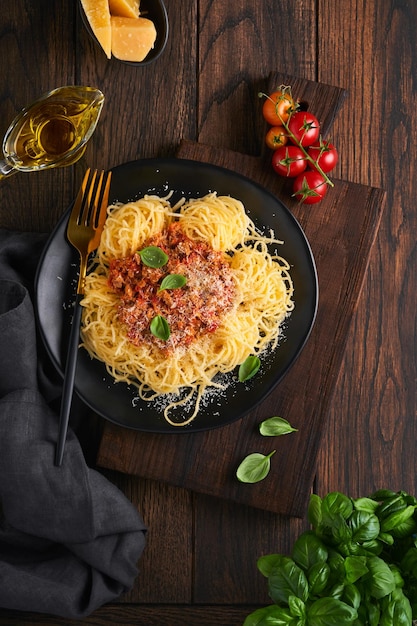 Pasta espaguetis a la boloñesa Sabrosos espaguetis italianos apetitosos con salsa boloñesa salsa de tomate queso parmesano y albahaca en plato blanco sobre fondo de mesa rústica de madera vieja Vista superior