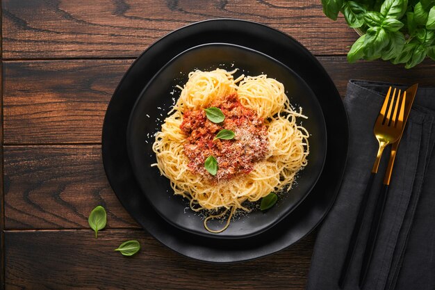 Pasta espaguetis a la boloñesa Sabrosos espaguetis italianos apetitosos con salsa boloñesa salsa de tomate queso parmesano y albahaca en plato blanco sobre fondo de mesa rústica de madera vieja Vista superior