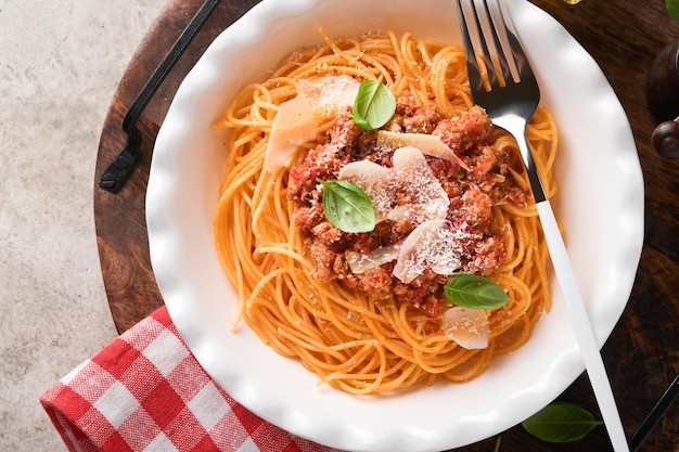 Pasta espaguetis a la boloñesa Sabrosos espaguetis italianos apetitosos con salsa boloñesa salsa de tomate queso parmesano y albahaca en plato blanco sobre piedra gris o fondo de mesa de hormigón Vista superior