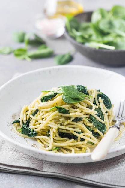 Pasta de espaguetis con espinacas y pesto verde, en un plato blanco sobre fondo de piedra gris