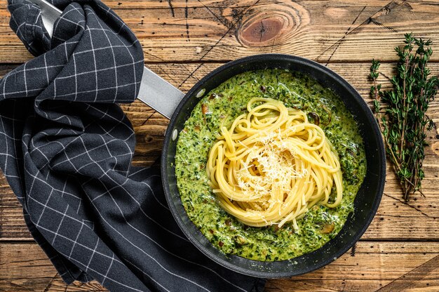 Pasta de espaguetis con espinacas en salsa de crema con parmesano en una sartén. Fondo de madera. Vista superior.