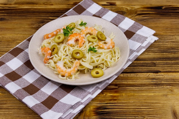 Pasta de espaguetis con gambas, aceitunas verdes y perejil sobre mesa de madera