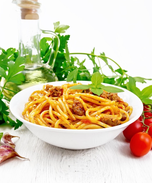 Pasta de espaguetis con salsa boloñesa de carne picada, jugo de tomate, ajo, vino y albahaca en un plato, aceite vegetal, hierba picante sobre un fondo de tablero de madera blanca