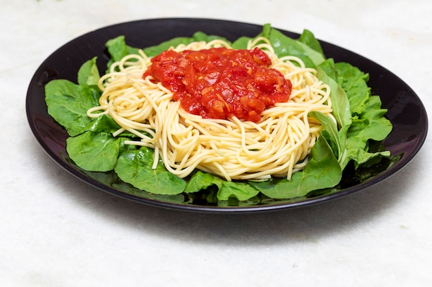Pasta de espaguetis con salsa roja y rúcula en placa negra con fondo de mármol blanco
