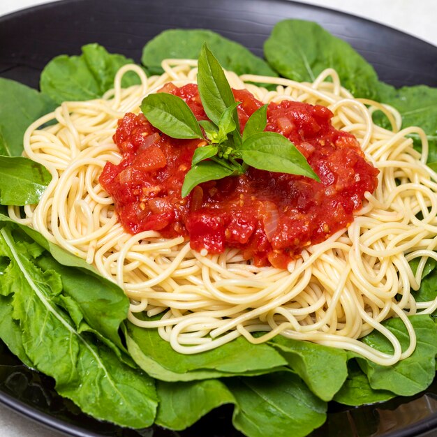 Pasta de espaguetis con salsa roja y rúcula en placa negra con fondo de mármol blanco