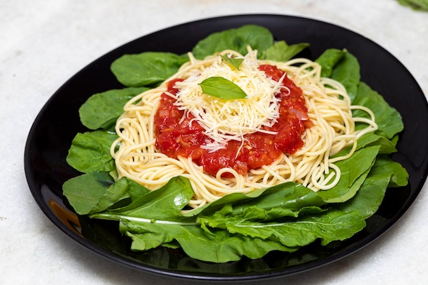 Pasta de espaguetis con salsa roja, rúcula y queso parmesano en placa negra con fondo de mármol blanco