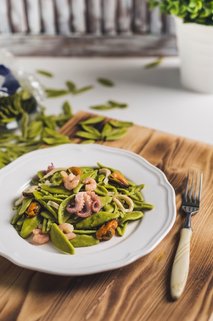 Pasta de espinacas con mariscos en un plato blanco sobre una tabla de madera