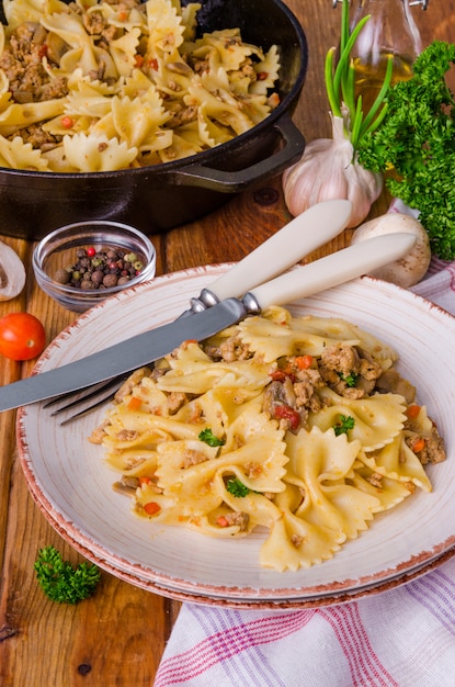 Pasta farfalle con carne frita, champiñones y verduras. Estilo rústico