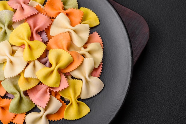 Pasta farfalle cruda en diferentes colores sobre un fondo de hormigón oscuro