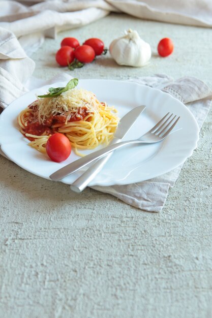 Pasta Fettuccine Bolognese mit Tomatensauce auf weißem Teller. Carlic und Salz und Tomaten auf einem konkreten Hintergrund mit Leinenservietten.