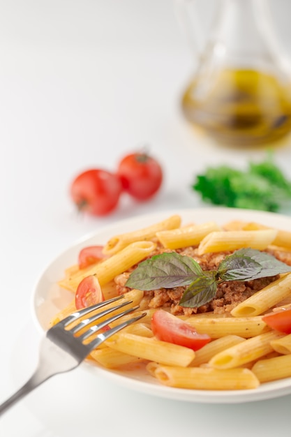 Pasta Fettuccine boloñesa con salsa de tomate y albahaca en plato blanco sobre blanco