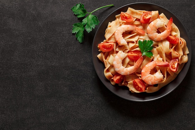 Pasta fettuccine con camarones y salsa de tomate en el espacio de vista superior de fondo oscuro para copiar texto