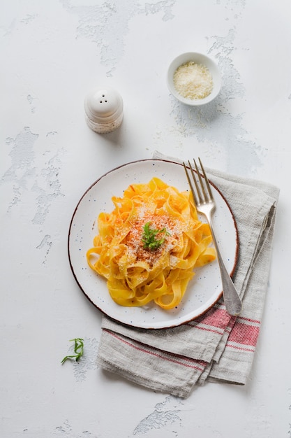 Pasta fettuccine con salsa Passat italiana tradicional y queso parmesano en placa de luz sobre superficie de hormigón blanco antiguo.